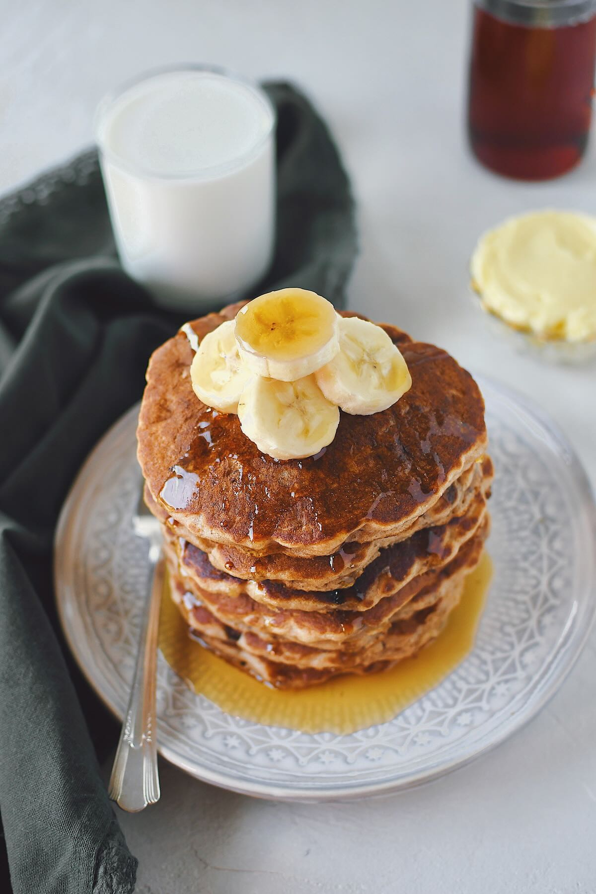 Banana Pancakes stacked high, topped with fresh banana slices, and drenched in maple syrup.