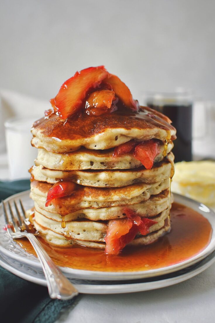 Rhubarb Pancakes stacked high and topped with cooked rhubarb and maple syrup.
