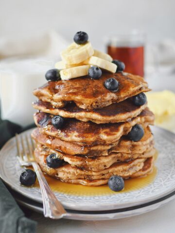 Blueberry Banana Pancakes stacked high, topped with banana slices and extra blueberries.