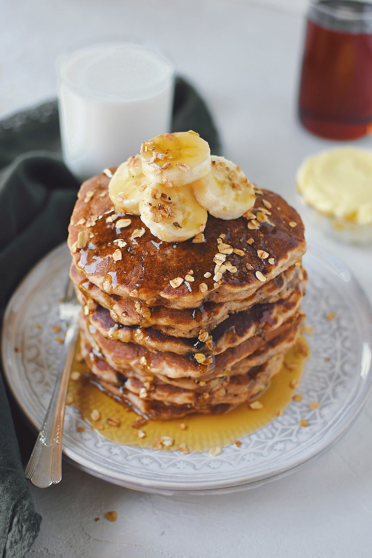 Banana Oat Pancakes stacked high, topped with banana slices and extra mini chocolate chips.