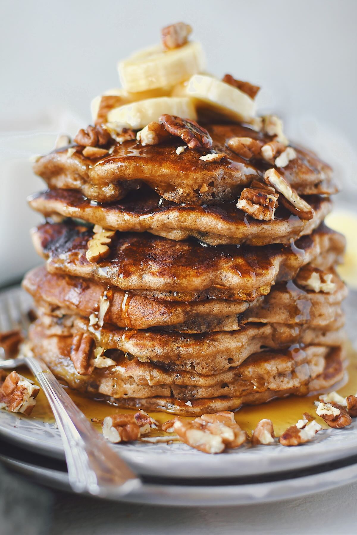Banana Pecan Pancakes stacked high, topped with banana slices and more chopped toasted pecans.