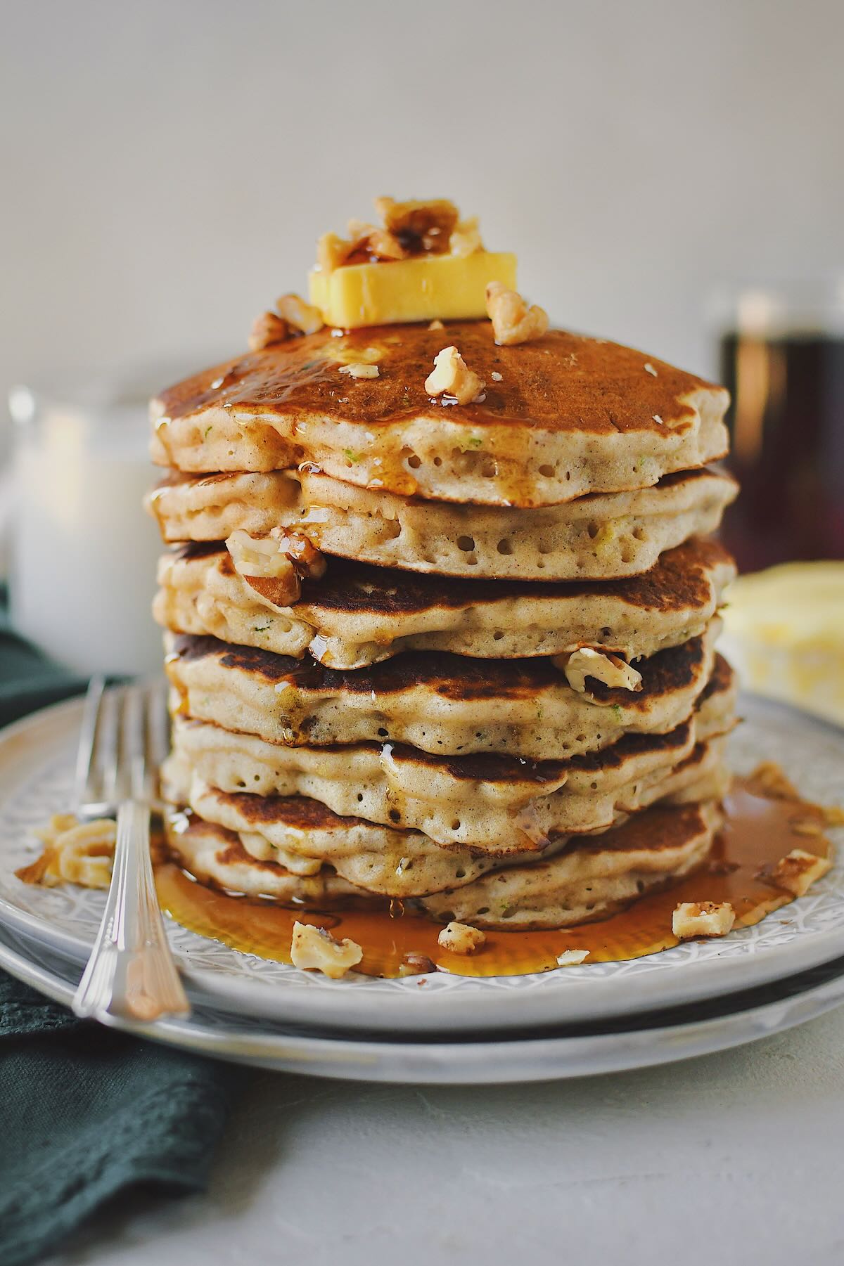 Zucchini Bread Pancakes stacked high and topped with a butter pat and extra walnuts.