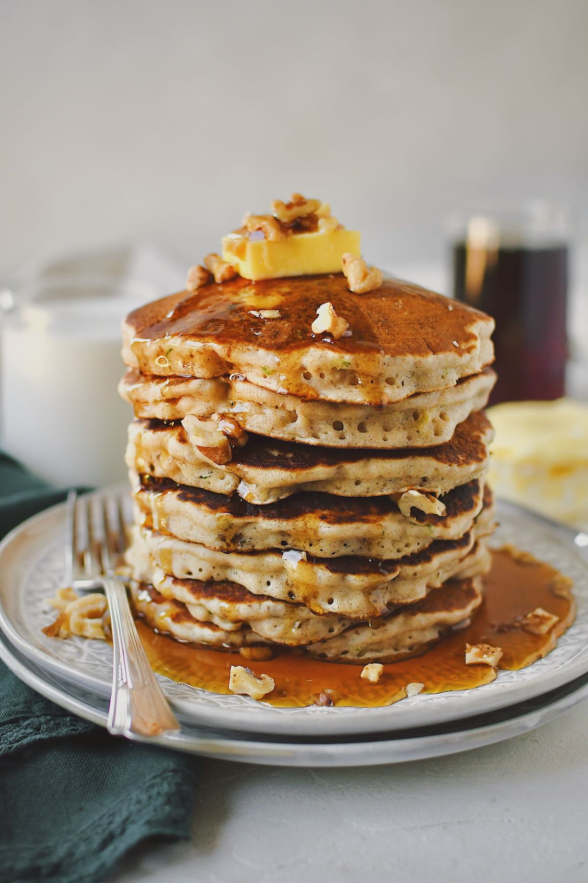 Zucchini Bread Pancakes stacked high and topped with a butter pat and extra walnuts.