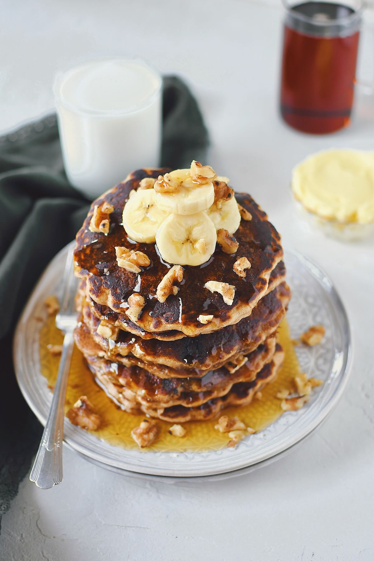 Banana Nut Pancakes stacked high, topped with banana slices and extra mini chocolate chips.
