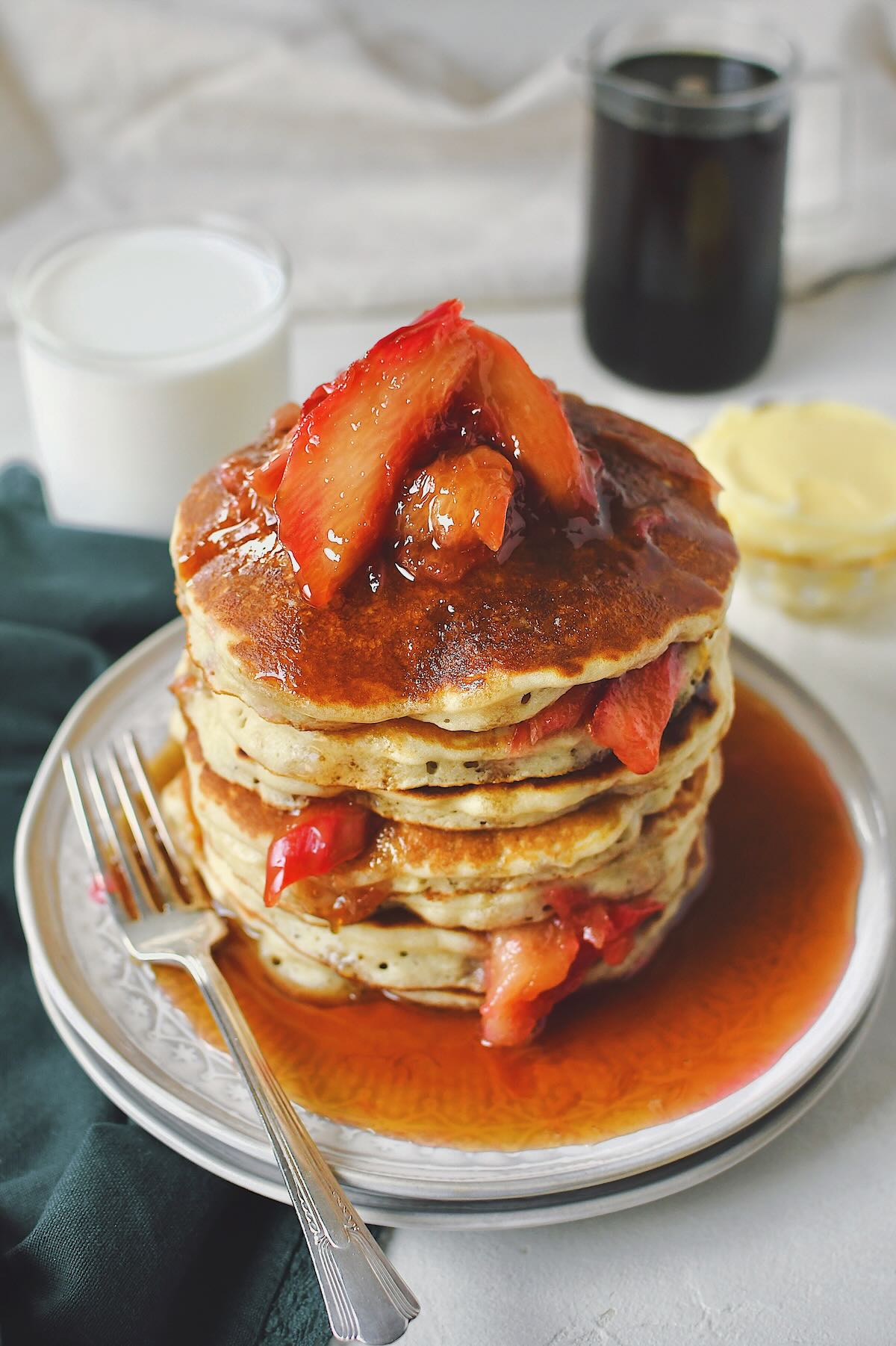 Rhubarb Pancakes stacked high and topped with cooked rhubarb and maple syrup.