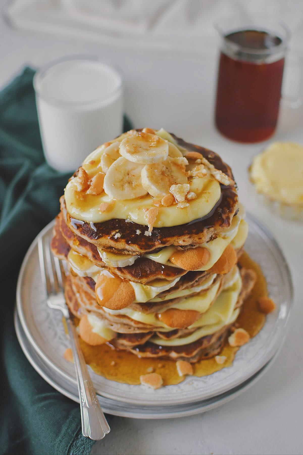 Banana Pudding Pancakes stacked up with pudding layered in between along with bananas and nilla wafers and finished with a drizzle of maple syrup.
