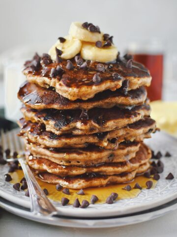 Banana Chocolate Chip Pancakes stacked high, topped with banana slices and extra mini chocolate chips.