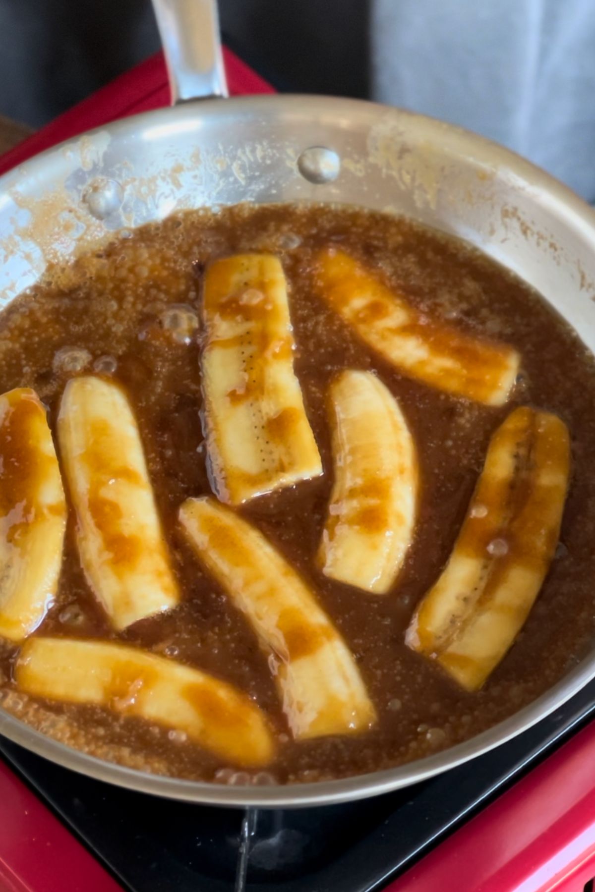 Bananas cooking in skillet in butter, brown sugar, and caramel sauce.