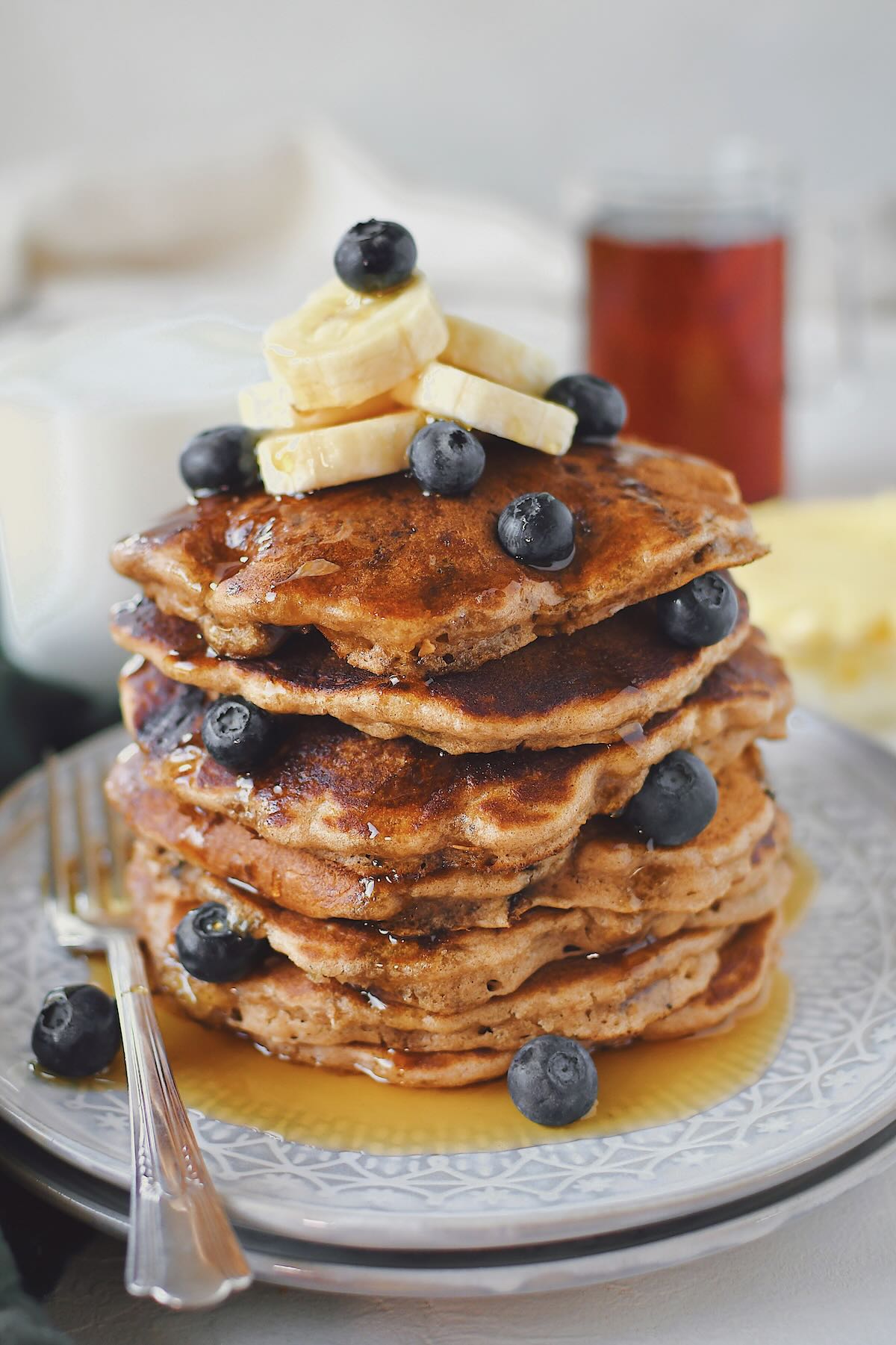 Blueberry Banana Pancakes stacked high, topped with banana slices and extra blueberries.