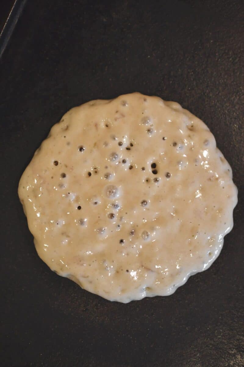 A pancakes cooking on a griddle, before flipping.