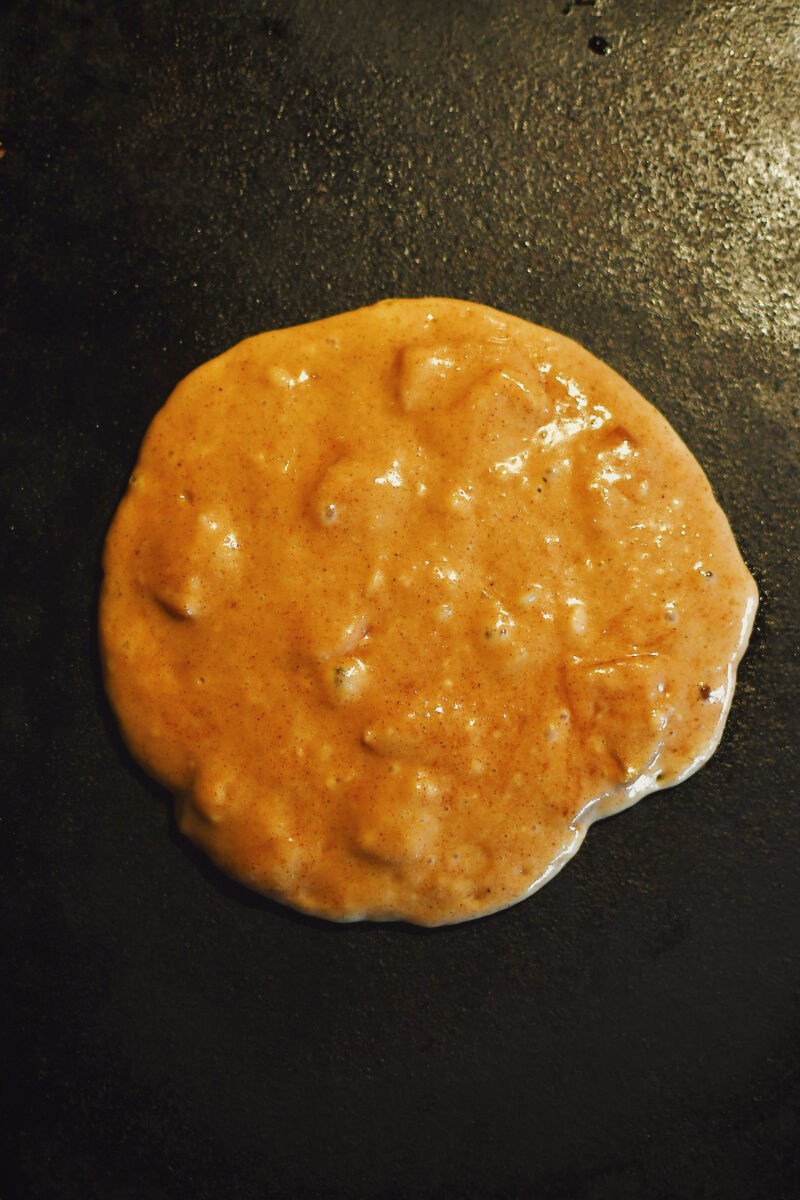 Apple Pancake batter cooking on a griddle, before flipping.