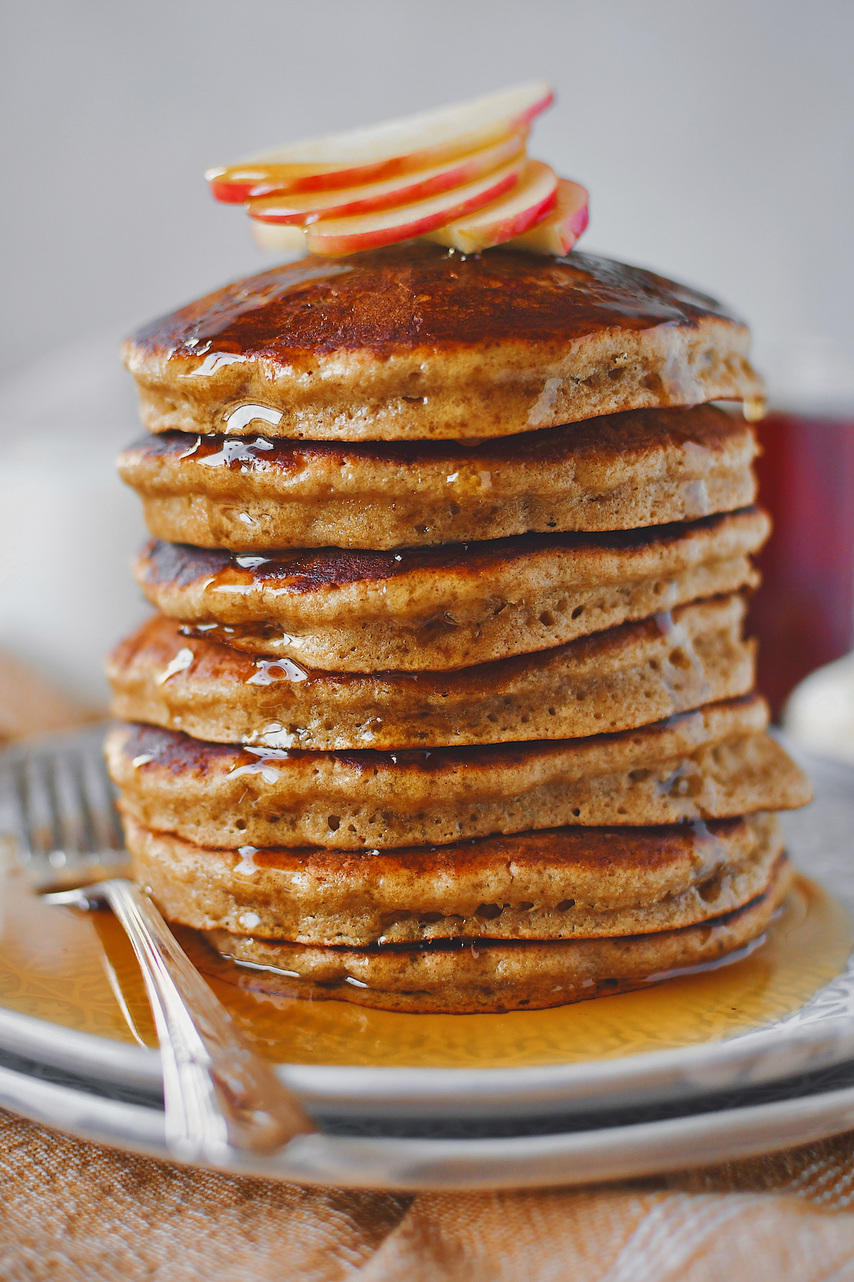 Apple Pancakes stacked high with a few slices of apple to garnish on top and drizzled in maple syrup!