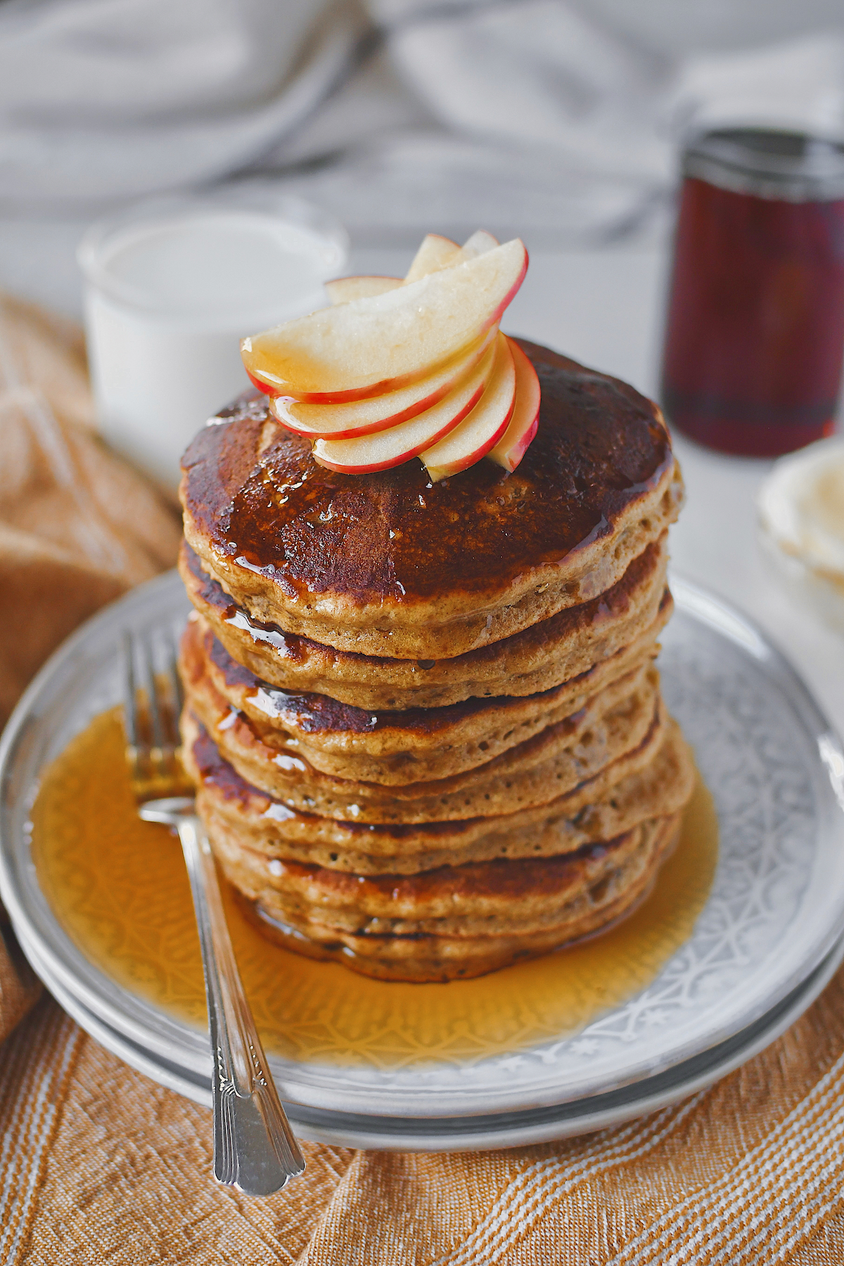 Apple Pancakes stacked high with a few slices of apple to garnish on top and drizzled in maple syrup!