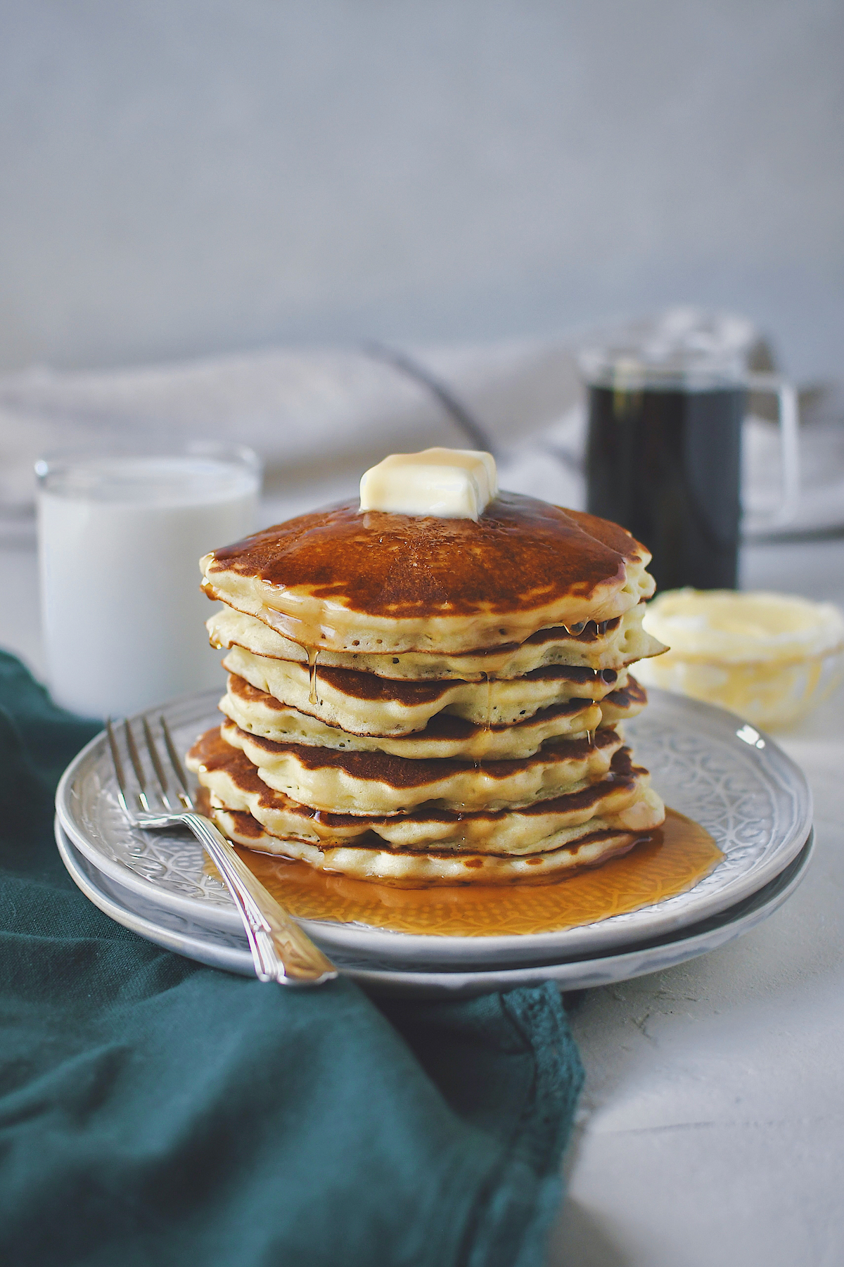 Fluffy Pancakes stacked up and topped with a pat of butter and drizzled in maple syrup.