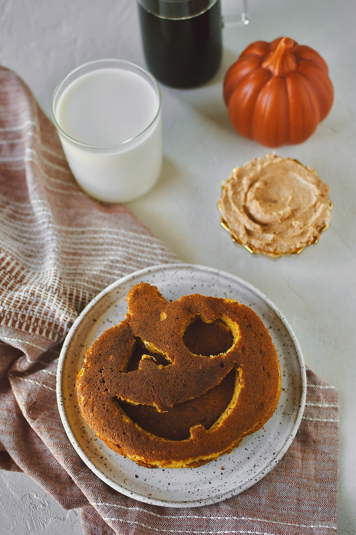 Jack-O-Lantern Pancakes on a plate, with a glass of milk on the side as well as some cinnamon butter and maple syrup.