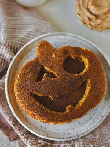 Jack-O-Lantern Pancakes on a plate, with a glass of milk on the side as well as some cinnamon butter and maple syrup.