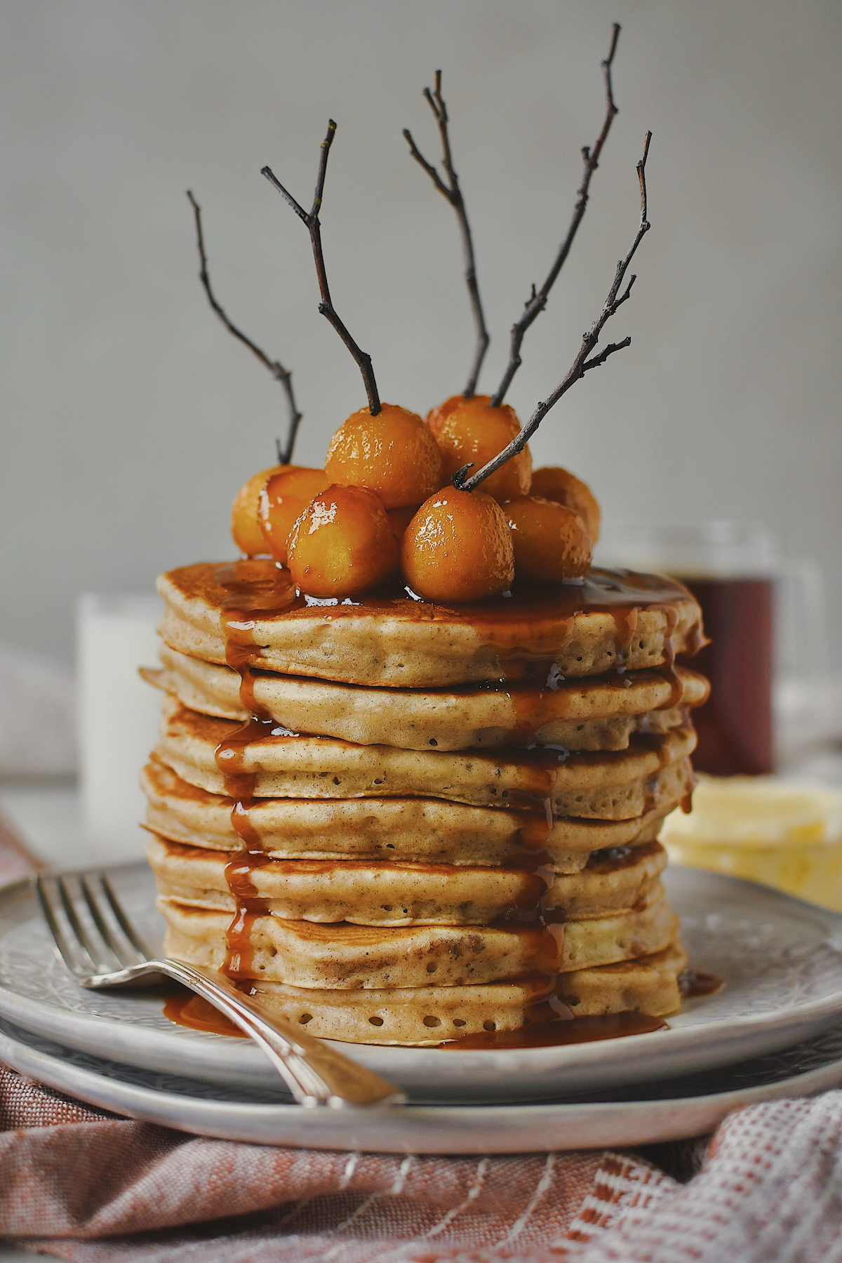 Caramel Apple Pancakes stacked high and topped with mini caramel apples and their sauce. Foraged twigs placed in some to mimic the sticks that come in traditional sized caramel apples.