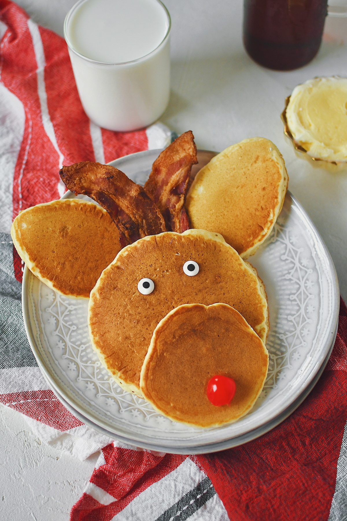 Reindeer Pancakes on a plate with bacon ears and a cherry nose, ready to be eaten.