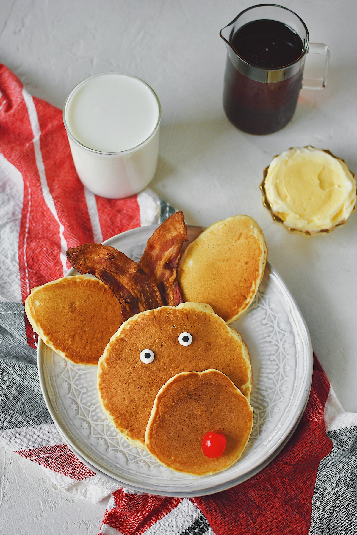 Reindeer Pancakes on a plate with bacon ears and a cherry nose, ready to be eaten.