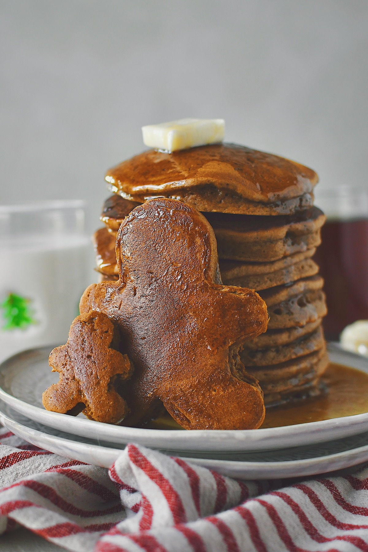Gingerbread Pancakes stacked high with two various sized ones in the front standing up, cut to look like undecorated gingerbread men.