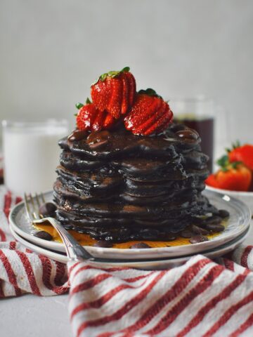 Chocolate Strawberry Pancakes stacked high, topped with sliced strawberries, extra chocolate chips, and a generous dose of maple syrup!
