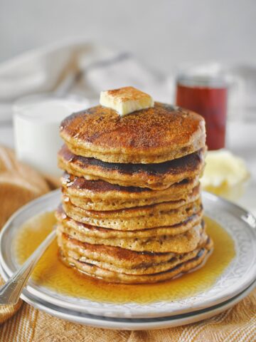 Apple Cinnamon Pancakes stacked high and topped with some butter, maple syrup, and a dusting of cinnamon.